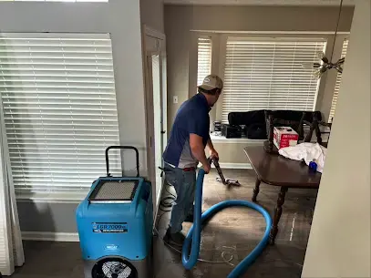 Technician running an extraction hose beside a dehumidifier in an Oak Ridge living room