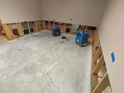Kernersville room with the lower drywall cut out and blue air movers drying the bare concrete floor